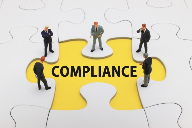 コンプライアンス COMPLIANCEと書かれたパズルとそれも見下ろすビジネスマンのミニチュアの人形