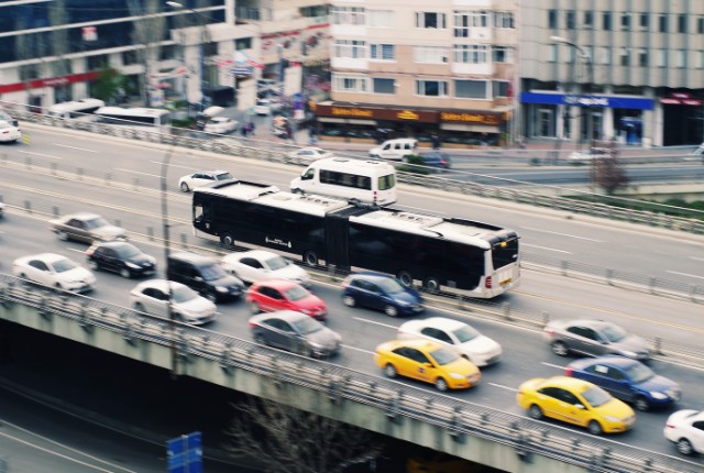 都市の高架道路を走る多くの車とバス。自動車運送業や交通量の多い都市部の物流を象徴する風景。