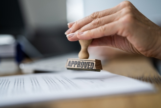 「APPROVED」と押された書類に判を押す手元。特定技能「漁業」人材の派遣申請承認のイメージ。
