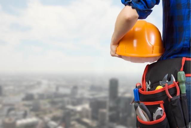 建設現場を背景に、安全ヘルメットを持つ作業員。特定技能フィリピン人の採用や建設業の人手不足対策をイメージ。