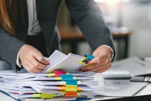 書類申請の準備 デスク上で大量の書類を整理するスーツ姿の人。外国人雇用に関する手続きや提出資料の準備を表すイメージ。
