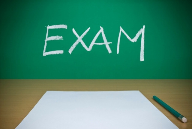 黒板に「EXAM」と書かれた教室で、白い用紙と鉛筆が置かれている試験準備のイメージ写真。
