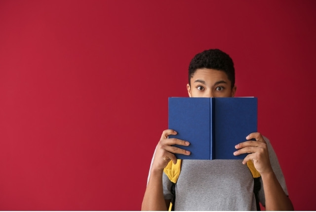 赤い背景の前で青い本を持ち、読書する若者。学習支援や日本語教育、特定技能試験対策の記事に適したイメージ。