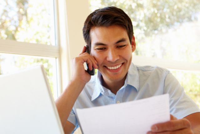 仕事中のフィリピン人男性 明るい部屋で書類を見ながら電話をする男性。採用担当者がフィリピン人の特徴や仕事観を理解するイメージ。