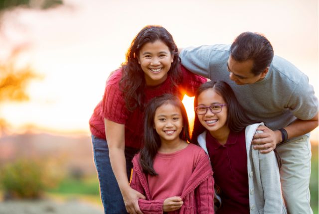 フィリピン人家族 夕日を背景に笑顔で寄り添う家族。フィリピン人の温かい家族愛や助け合いの文化をイメージした写真。