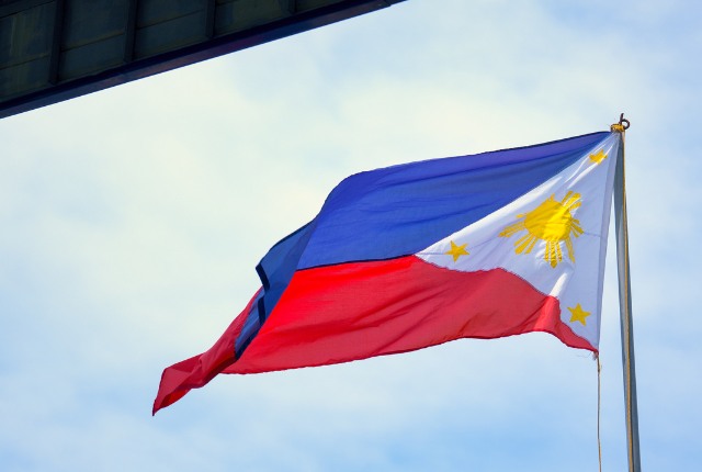 旗 青・赤・白の三色と太陽のデザインが特徴のフィリピン国旗が、青空の下で風にはためいている様子。