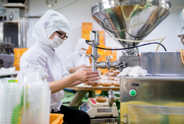 工場で働く特定技能外国人 食品工場で衛生服を着た作業員が充填機を使い容器に製品を詰める様子。飲食料品製造業の現場。