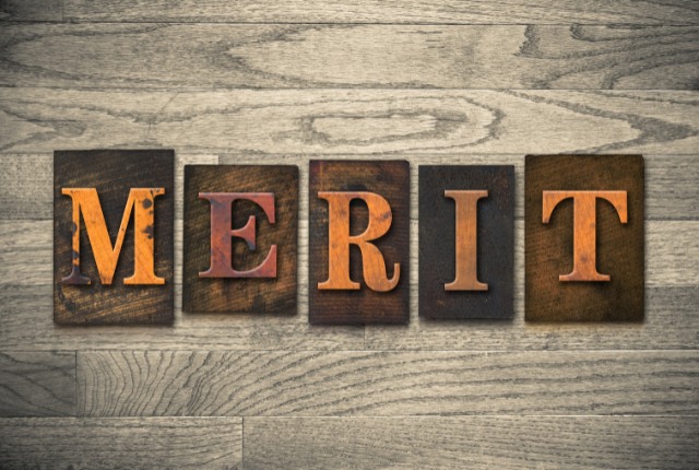 メリット 木目の背景に「MERIT」と刻まれたビンテージ風の文字ブロックが並ぶ。利点やメリットを表現するイメージ。