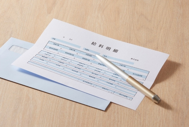 給与明細と封筒、ボールペンが机の上に置かれている写真。給与管理や外国人材の雇用手続き、労務関連の記事に適した画像。