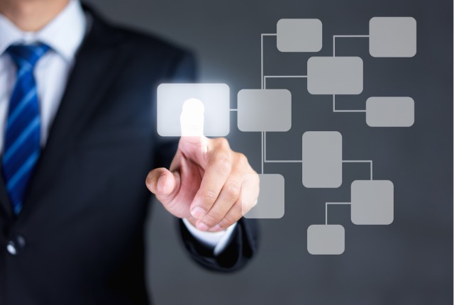 スーツ姿の男性が組織図を指し示すイメージ。造船業における特定技能外国人の採用体制や管理を表現。