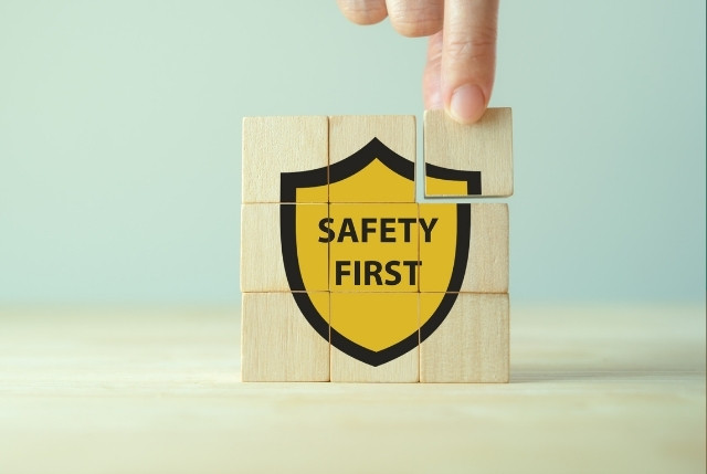 「SAFETY FIRST」と書かれた盾マークを積み木で組み立てる手。漁業現場での安全管理や労働安全対策の象徴。
