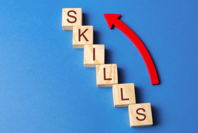 スキルアップ 木製ブロックで「SKILLS」と並び、上向き矢印が描かれた画像。スキルアップや人材育成を象徴するビジュアル。