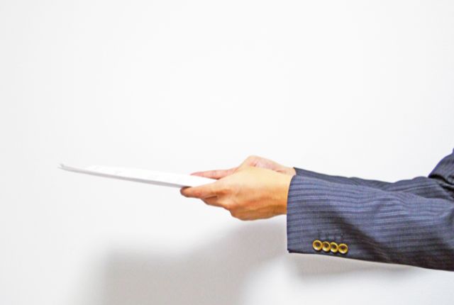 手続き書類の提出 スーツ姿の人が書類を差し出す様子。外国人雇用に関する届出や申請書類の提出をイメージした写真。