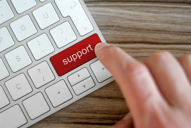 キーボードの赤い「support」キーを指で押す様子。企業のサポート体制をイメージ。