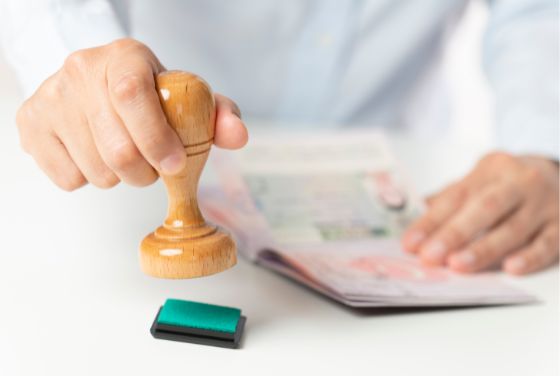 木製スタンプを使ってパスポートに押印する様子。ビザ取得や日本入国手続きをイメージした行政手続きの場面。