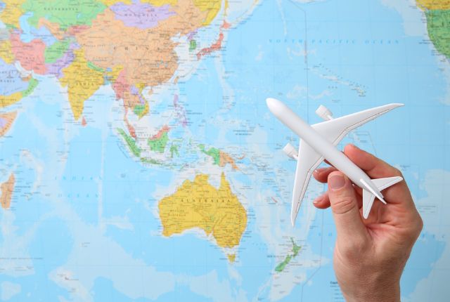世界地図を背景に飛行機の模型を持つ手の写真。航空業界の採用を連想させるイメージ。