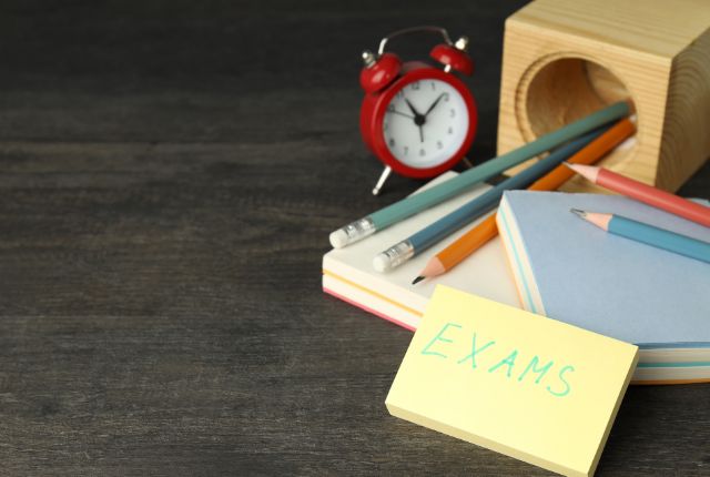 試験準備を示す文房具とメモの写真。鉛筆、付箋、時計が置かれた学習・試験対策のイメージ。