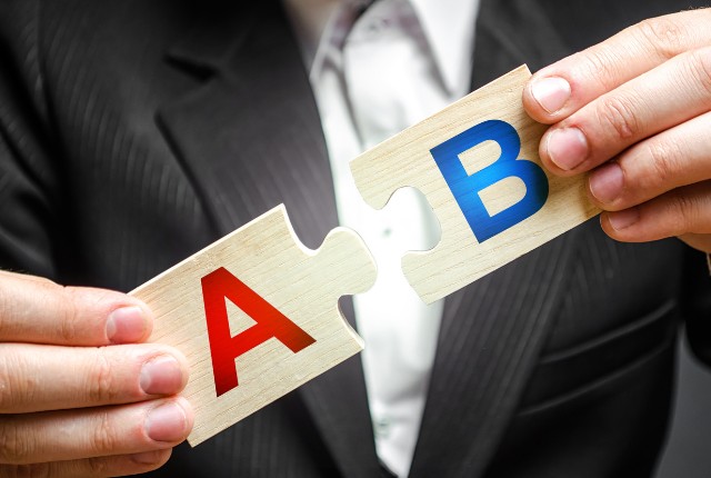 スーツ姿の男性が「A」と「B」と書かれたパズルのピースを組み合わせている。外国人雇用や助成金制度の比較を表すイメージ。