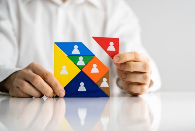 人のアイコンが描かれたカラフルな図形ブロックを組み合わせる手元の写真。人材配置や組織構成のイメージ。