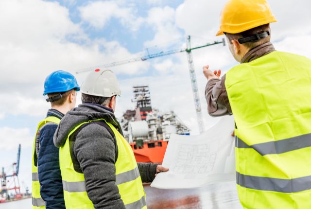 造船現場で作業員が図面を確認しながら船舶建造を指示する様子。特定技能2号の業務内容を示すイメージ。