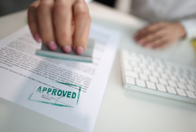 書類に「APPROVED」の承認印を押す手元の写真。新卒外国人採用や留学生の在留資格申請が許可される場面のイメージ。