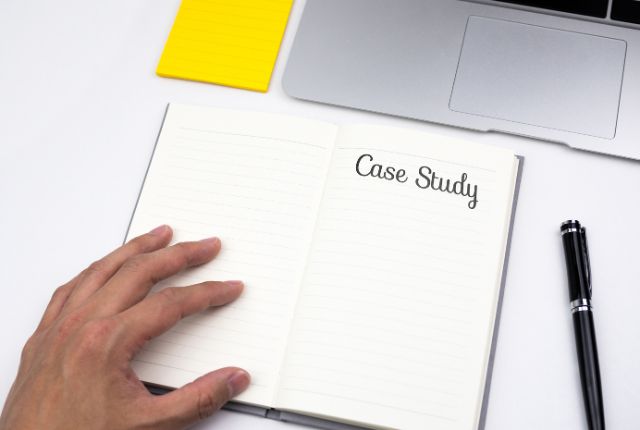 ノートに「Case Study」と書かれたページを開き、手が添えられている写真。事例紹介や分析を示すイメージ