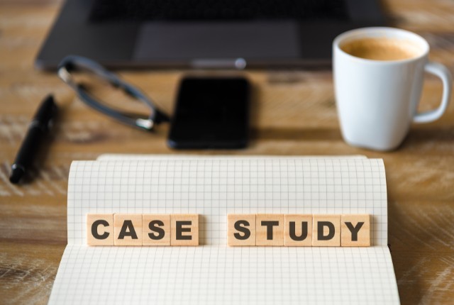 ノートの上に「CASE STUDY」と並べられた木製ブロック。背景にパソコンやコーヒーがあり、助成金活用事例の紹介を表すイメージ。