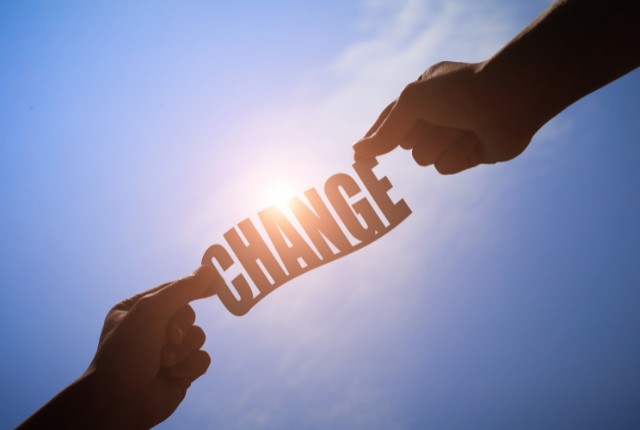 青空の下で“CHANGE”の文字を持つ二人の手。送り出し機関の変更を象徴するイメージ写真