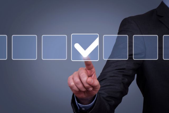 ビジネススーツの人物がチェックマークをタッチし、認定を示すイメージ。審査・評価の象徴的シーン。