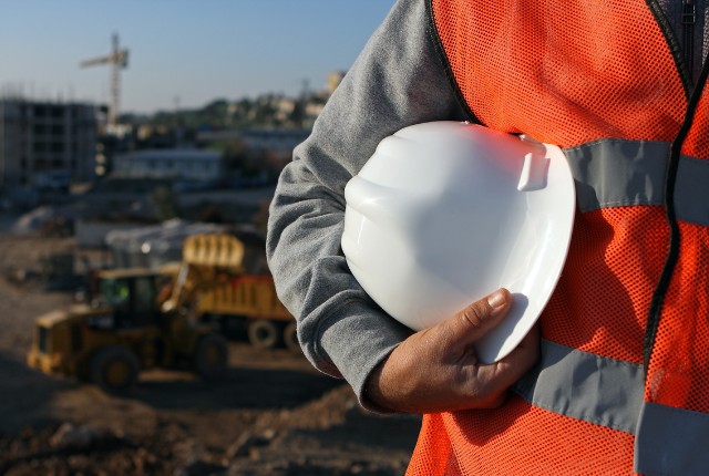 建設現場で白いヘルメットを手に持つ作業員の写真。特定技能や安全管理、建設業の現場イメージに適した画像。