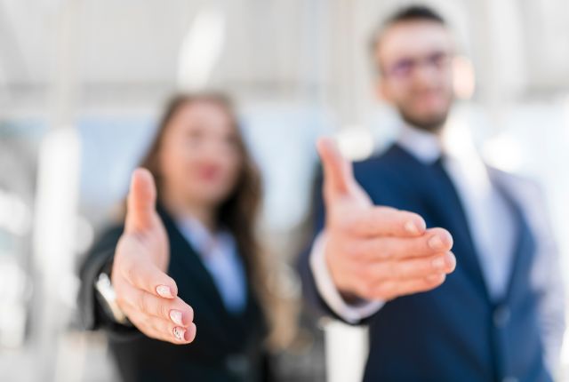 スーツ姿の男女が前に手を差し出す写真。握手や歓迎、ビジネスパートナーの関係構築をイメージしたシーン。