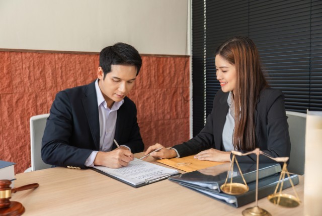 オフィスで書類に署名する男女ビジネスパーソン。外国人雇用契約や在留資格申請のコンサルティングを進める場面のイメージ。