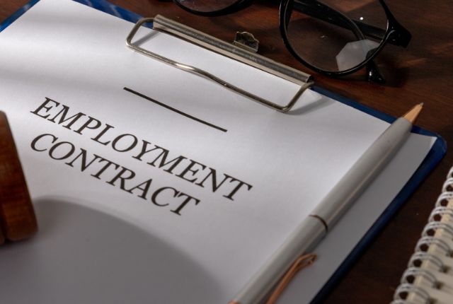 雇用契約書とペン、眼鏡が机の上に置かれた様子。雇用条件や契約手続きのイメージ。