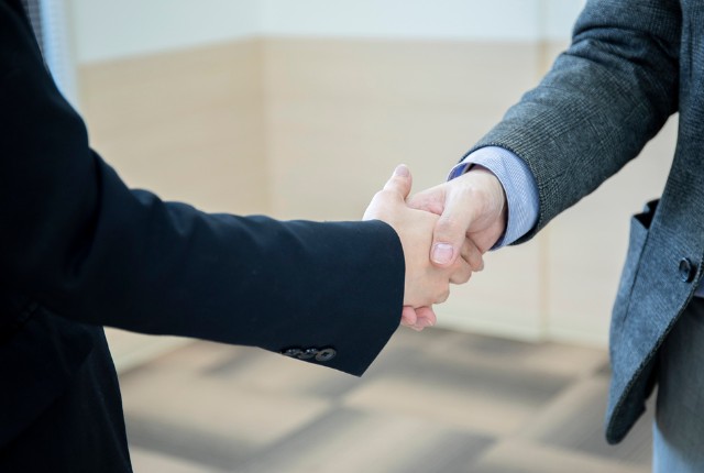 スーツ姿のビジネスパーソン同士が握手を交わす様子。送り出し機関変更後の新たな協定や契約締結を表すイメージ
