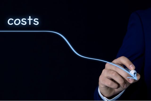 ビジネススーツの手がコスト削減を示す下向きのラインを描く様子の写真。経費削減やコスト最適化のイメージ。