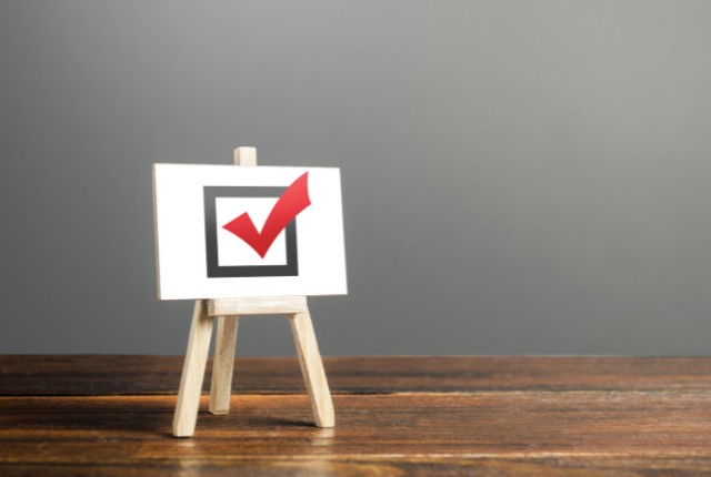 木製イーゼルに赤いチェックマーク入りのボードが立てられている様子。外国人技能実習制度やJITCOの役割を象徴。