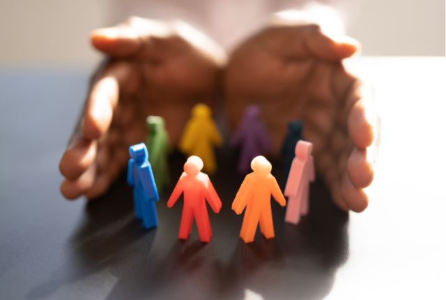 両手に守られるように円形に並んだカラフルな人型フィギュアの画像。多様性や人材支援を表すイメージ。