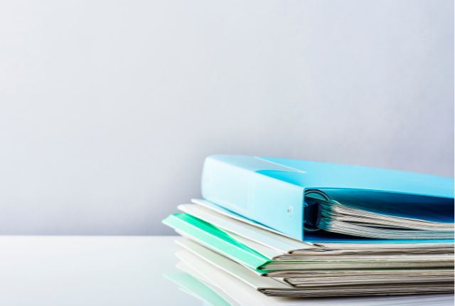 必要書類 書類が入った青と緑のファイルが机の上に積まれている様子。ビザ申請や雇用手続きに関する資料をイメージさせる構図。