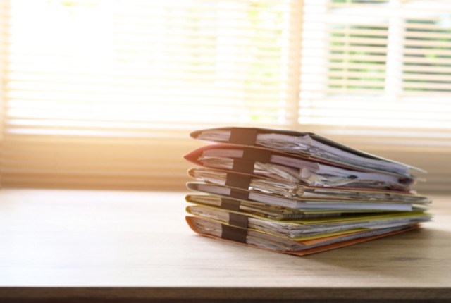 机の上に積まれた申請書類の束。特定技能2号の在留資格変更や農業分野の手続き書類をイメージ。