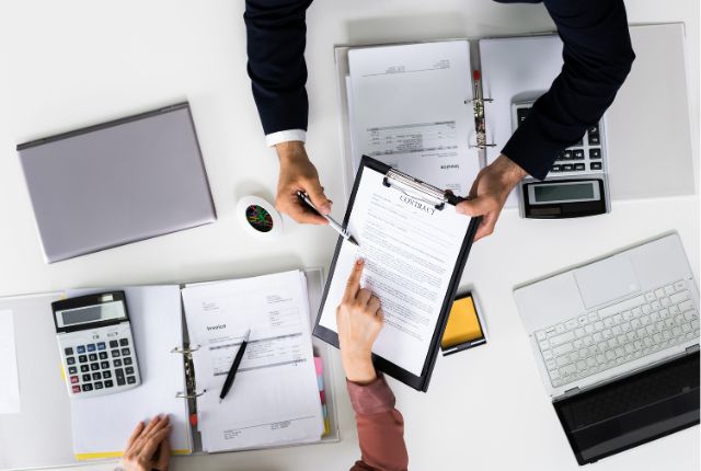 書類の準備 DMV申請書類を確認するビジネスパーソンたちのデスク上のやり取り。外国人雇用の手続きや書類管理のイメージ。