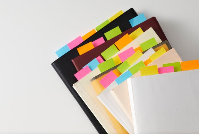 カラフルな付箋が貼られた複数のファイルや資料の写真。送り出し機関の選定基準や必要書類の整理をイメージできる構図。