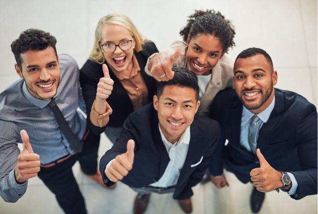 笑顔で親指を立てる多国籍のビジネスチーム。外国人雇用やダイバーシティ推進の成功を表すイメージ。