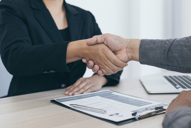 外国人との雇用契約 外国人雇用の面接で握手するビジネスパーソン。採用契約や在留資格手続きの成功を象徴する場面。