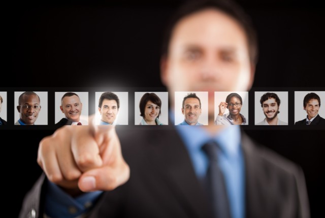 外国人の雇用プロセス 多様な人材の顔写真を指で選択するビジネスパーソン。グローバル採用や外国人雇用を象徴するイメージ。