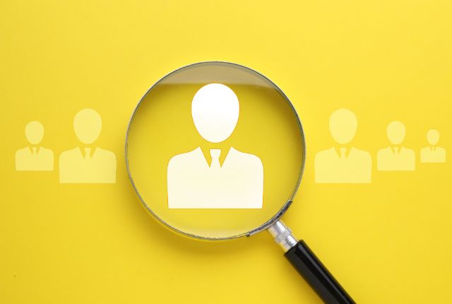 外国人採用を示す人物アイコンを虫眼鏡で拡大するイメージ。企業の採用判断やメリット・デメリットを表すビジュアル