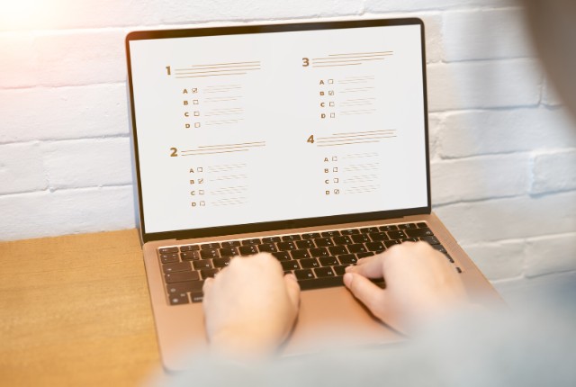 ノートパソコンでオンライン試験を受ける人の手元。画面には選択式の問題が表示され、技能評価テストや筆記試験をイメージ。
