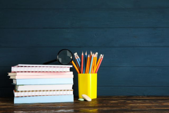 木の机の上に積まれたノートと、黄色のペン立てに入った鉛筆や消しゴム。学習や試験準備のイメージ。