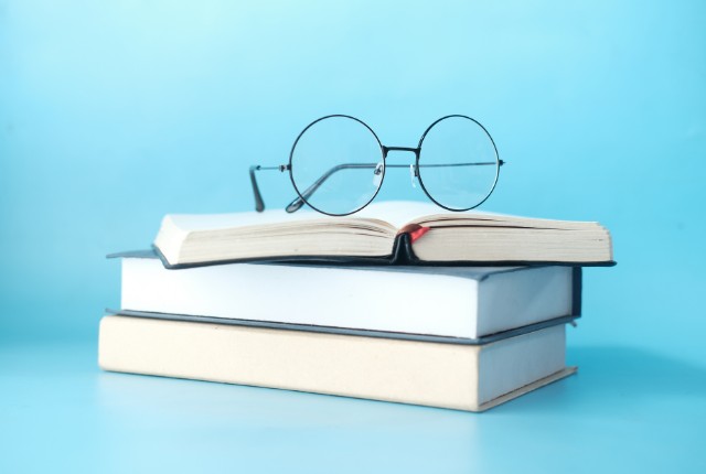 開いた本と丸眼鏡が重ねて置かれている。特定技能試験や日本語能力試験の学習を象徴するイメージ。