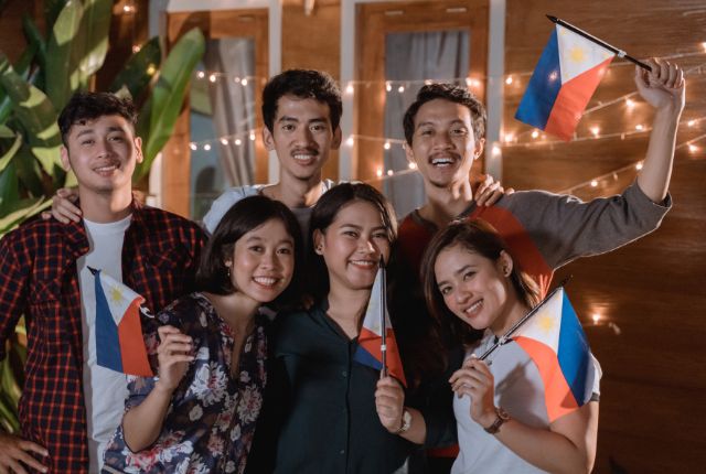 フィリピン国旗を持つ若者たちが笑顔で集まっている写真。外国人コミュニティや多文化交流を示すイメージ。