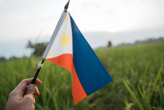 農地でフィリピン国旗を手に持つ様子。日本の農業分野で働くフィリピン人特定技能2号人材の象徴。